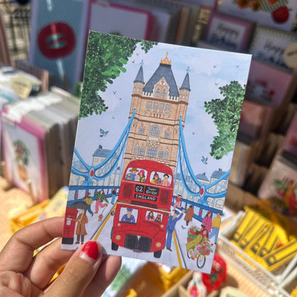 Illustrated Tower Bridge postcard showing red London bus, cyclists and cat in a jumper, London souvenir postcard by The Mundane Gift Shop