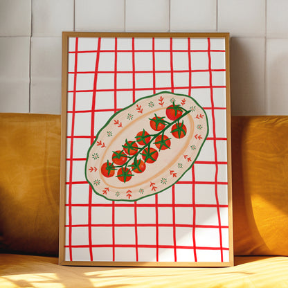 Framed artwork with a design of tomatoes on a white background with red grid lines, leaning against a textured wall.