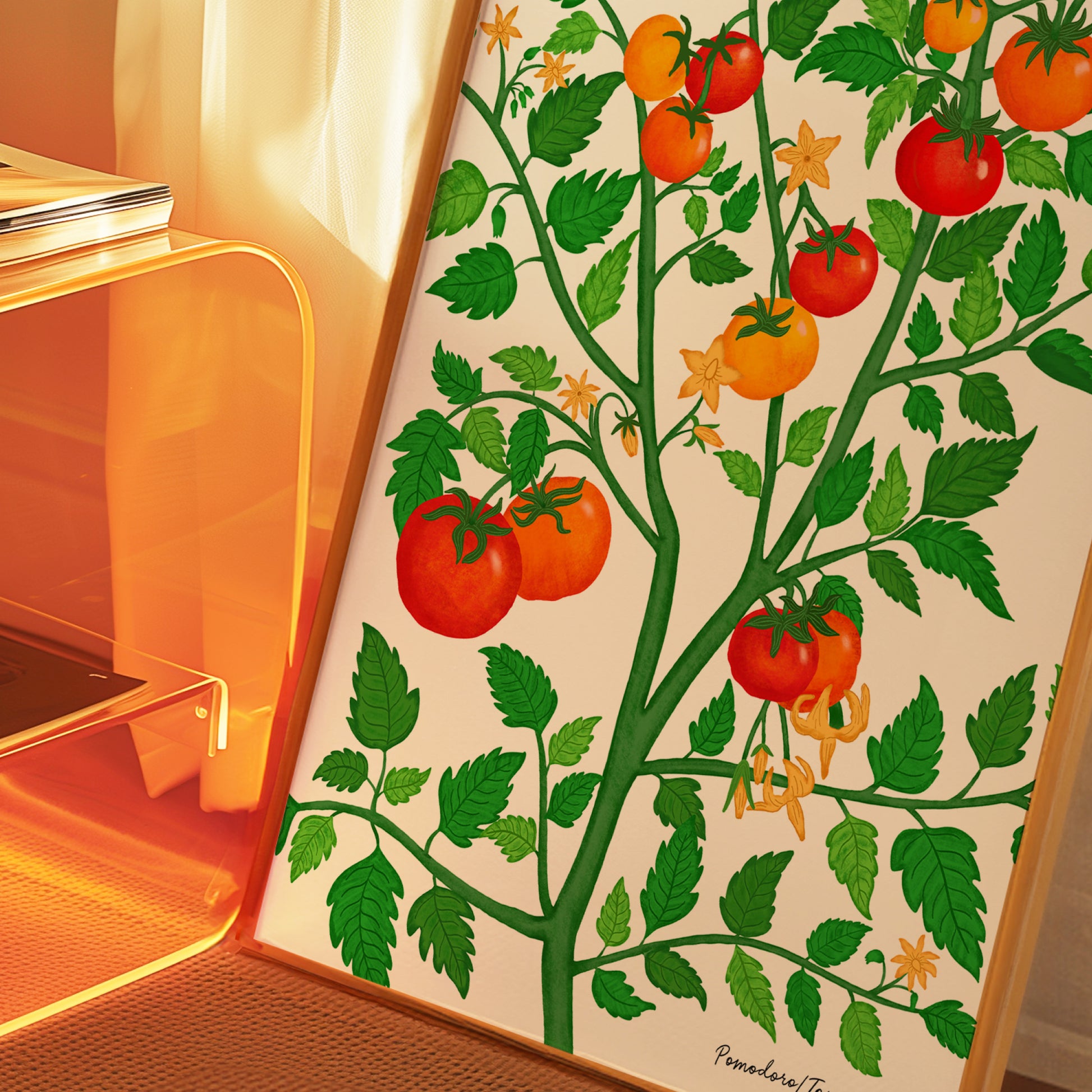 A framed botanical art print of a tomato plant with green leaves and red and orange tomatoes, leaning against a glass side table in warm, orange-toned ambient light.